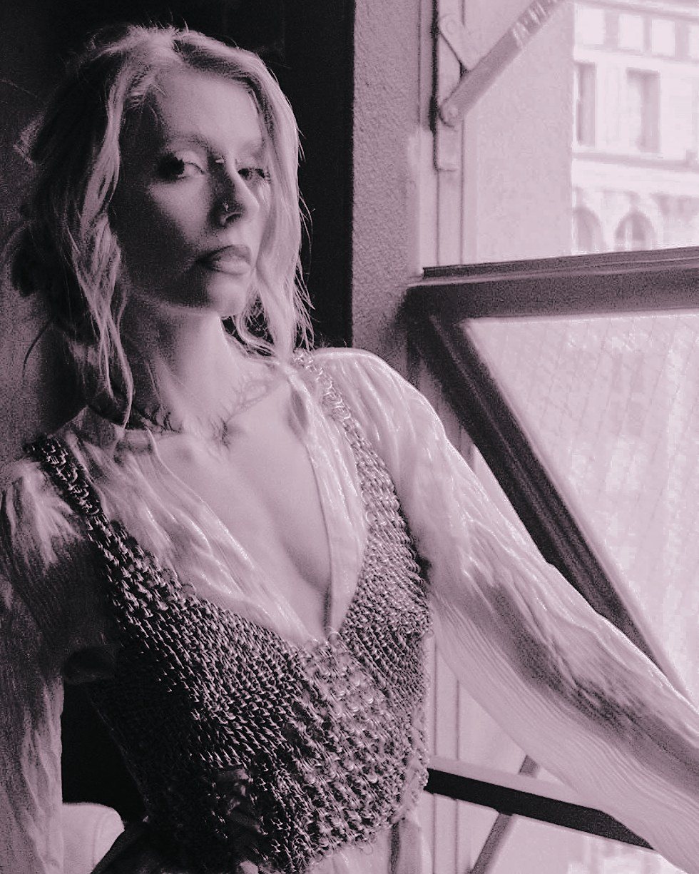 Krista by a downtown window in a chainmail bodice laced with ribbon over a sheer white blouse