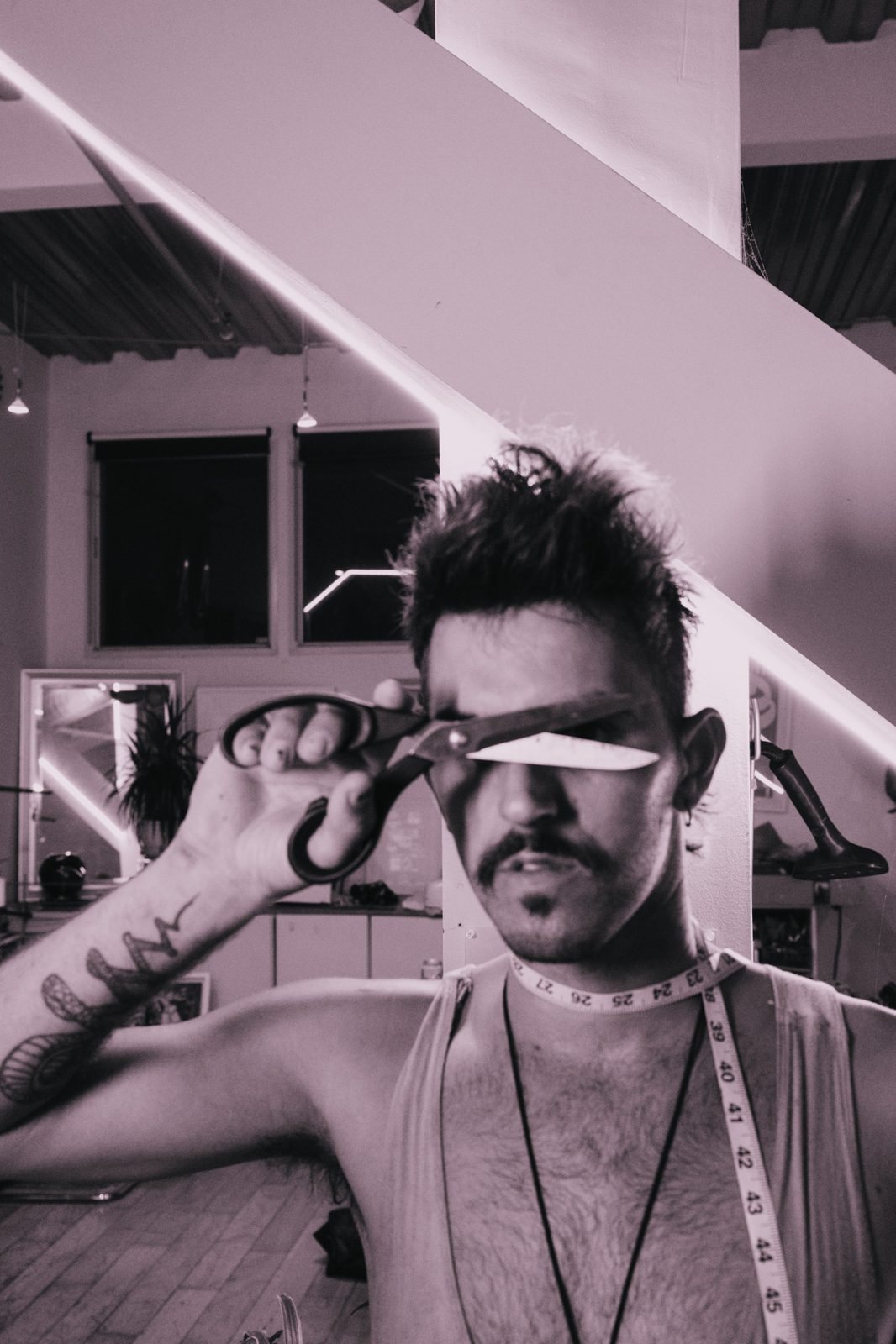 Designer with a tape measure around his neck holding shears across his eyes