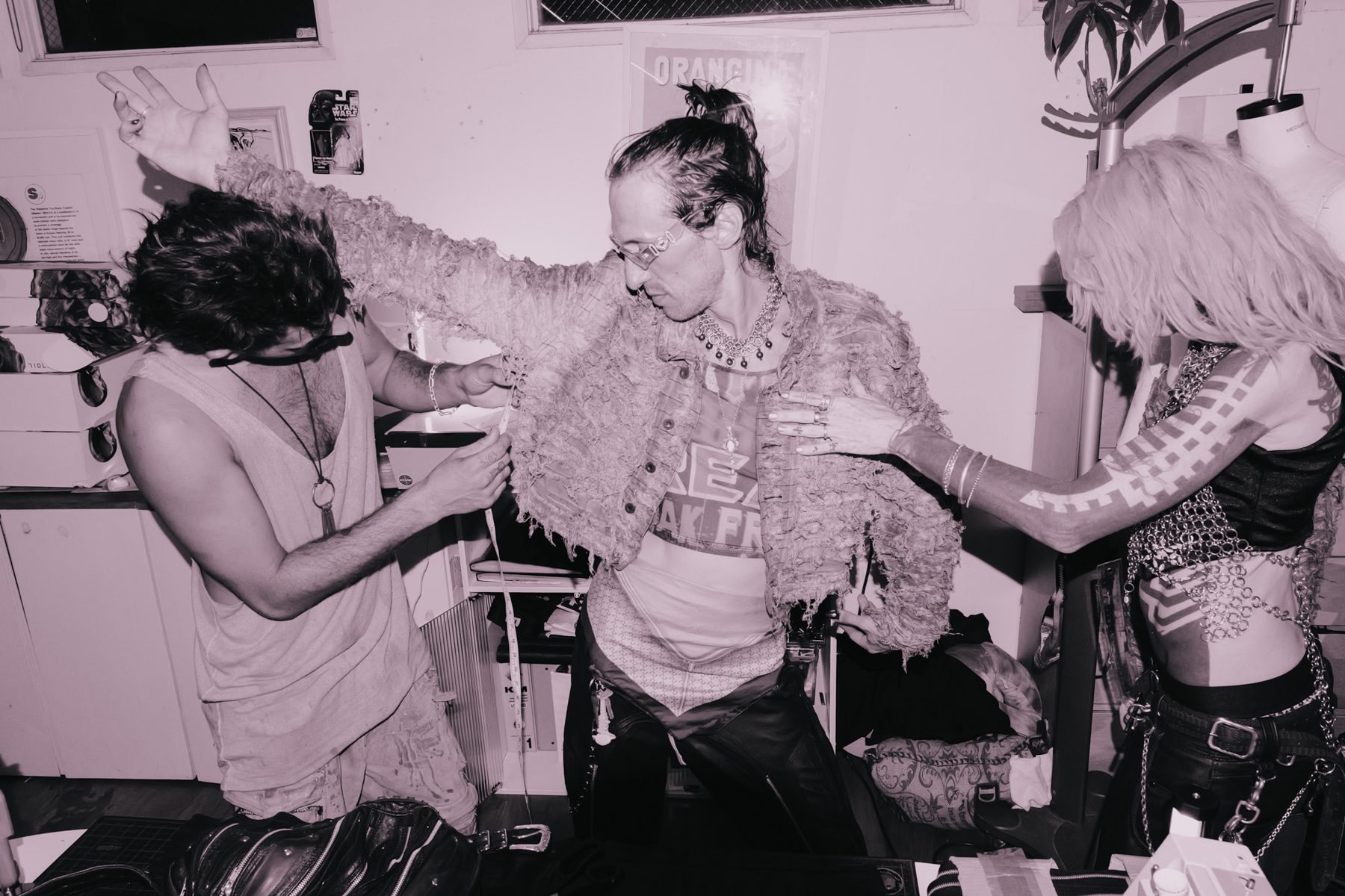 Two designers measuring and pinning a shredded jacket on a model with his arm raised
